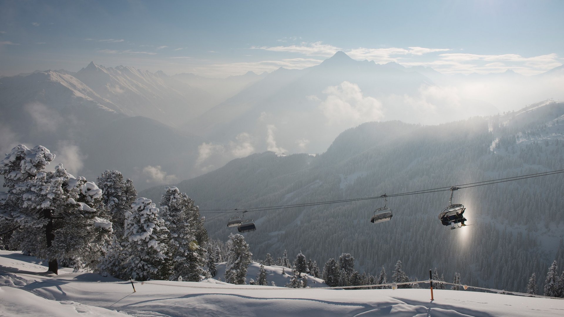 Skilift in den Bergen Skilift fährt über eine verschneite Winterlandschaft mit Blick auf die umliegenden Berge bei leichtem Nebel.