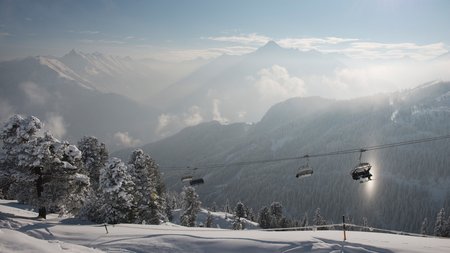 Seilbahn über verschneiten Bergen Seilbahn fährt über eine verschneite Berglandschaft mit Blick auf die umliegenden Gipfel bei leichtem Nebel.