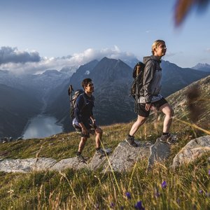 Wanderung in den Bergen Zwei Wanderer steigen einen Bergpfad hinauf mit einem malerischen Bergsee und Berggipfeln im Hintergrund.
