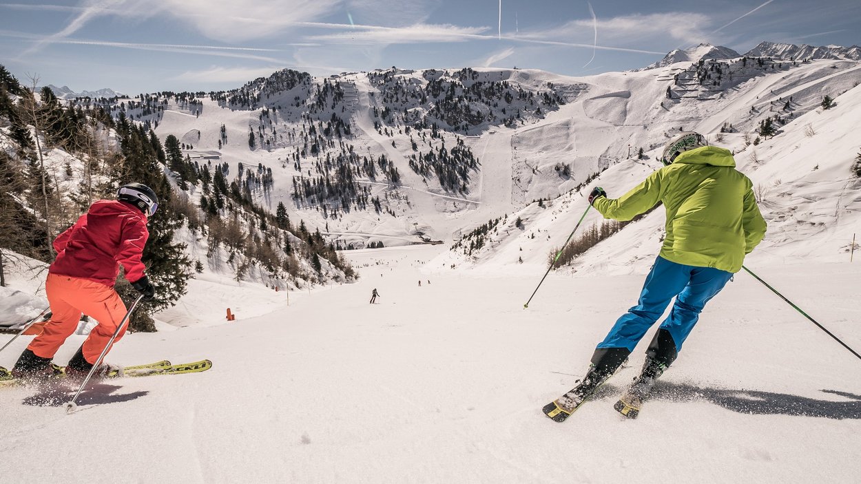Skifahren im größten Skigebiet Österreichs – Winterspaß in den Alpen Zwei Skifahrer auf einer schneebedeckten Piste im größten Skigebiet Österreichs, umgeben von alpinen Bergen und klarer Winterlandschaft.
