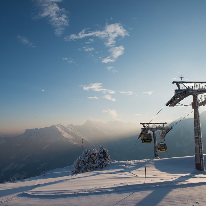 Seilbahn bei Sonnenuntergang Seilbahn fährt über eine verschneite Berglandschaft bei Sonnenuntergang mit Blick auf die umliegenden Gipfel.